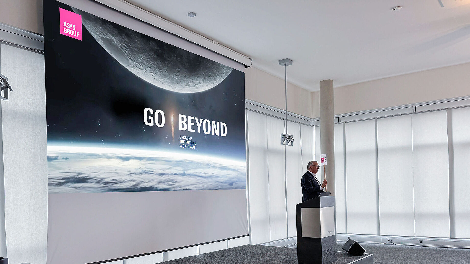 A man on a stage presenting from behind a lectern.