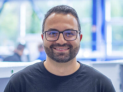 Smiling man standing in front of a machine line in a production hall.