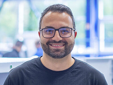 Ein lächelnder Mann steht vor einer Maschinenlinie in einer Produktionshalle.