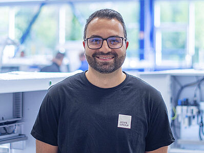 Smiling man standing in front of a machine line in a production hall.