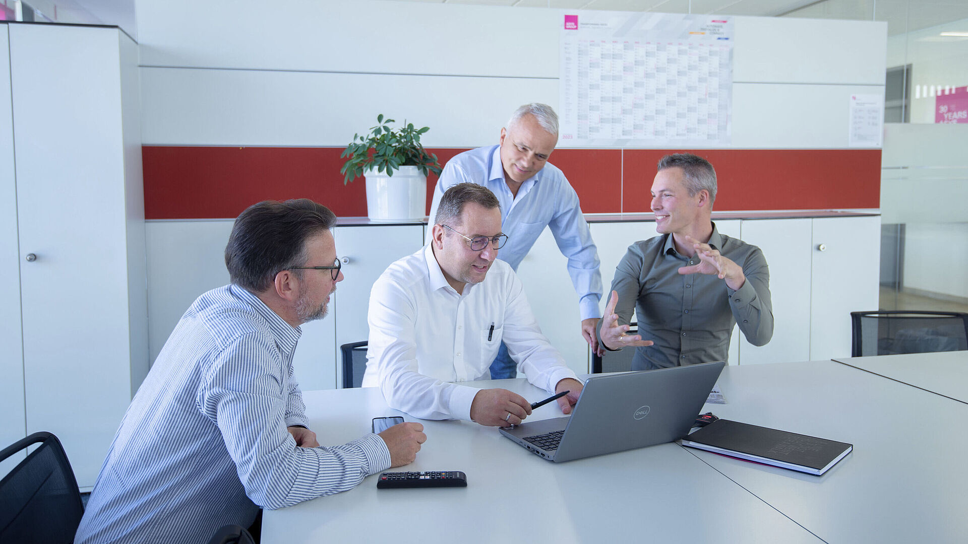 Vier Männer stehen/sitzen um einen Laptop herum und diskutieren