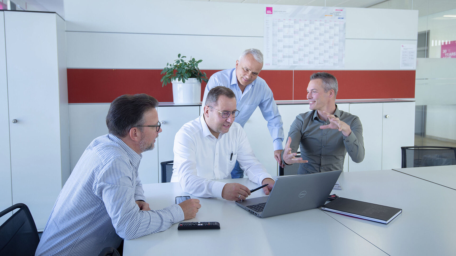 Four men are standing/sitting around a laptop and discussing something.