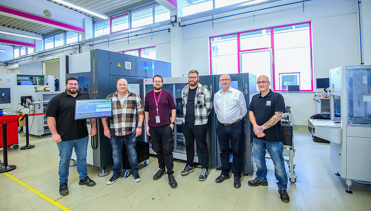 Six men are standing side by side, smiling, in front of a panel saw.