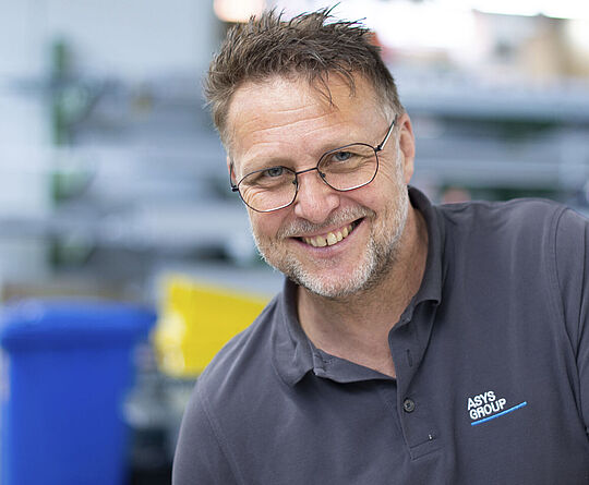 A man is standing in a production hall, smiling.