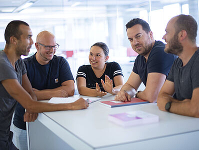 Fünf Personen stehen gemeinsam an einem Stehtisch und diskutieren miteinander.