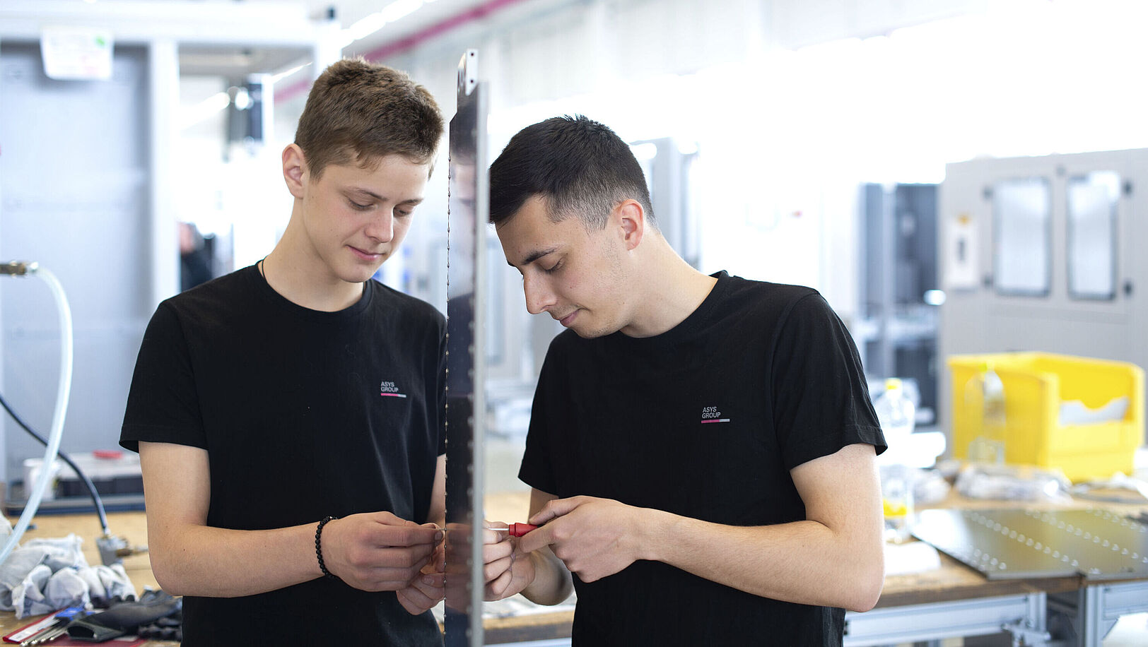 Two boys are working with screws on a vertically positioned panel.