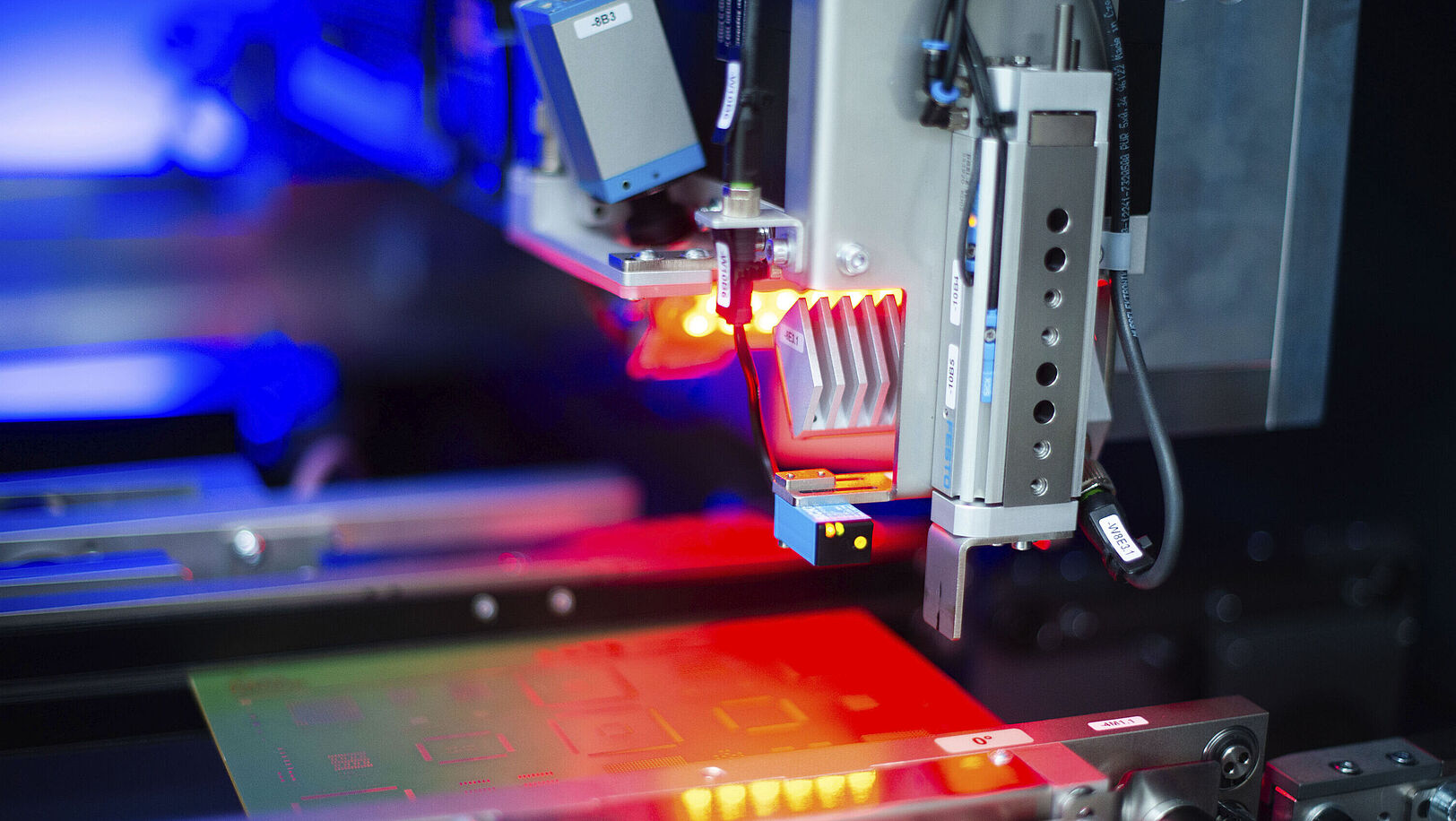 Interior view of a laser machine, red light illuminating an inserted circuit board.