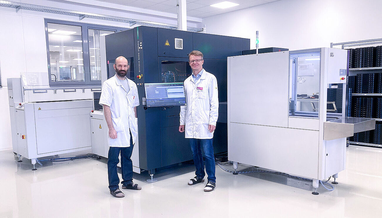 Two men in white lab coats are standing in front of sheet-cutting machines.