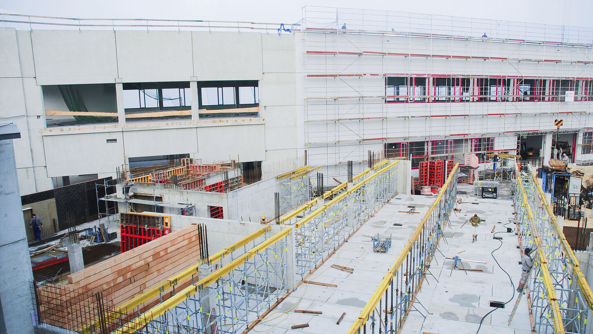 Draufsicht auf eine Baustelle zur Gebäudeerweiterung, mit sichtbaren Baugeräten und strukturellen Elementen. Jahr 2008